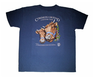 A navy blue shirt with artwork in the center depicting the heads of two shaggy brown cows with horns, wearing blue halters. On the right side of one cow is a viney wreath with small clusters of purple and blush flowers. White text around art reads “Common Ground Country Fair '' and  “Celebrate Rural Living with MOFGA”. A white MOFGA logo is in the bottom right corner. 